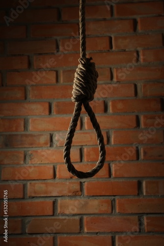 Rope noose with knot hanging near brick wall