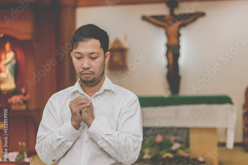 Asian man praying in a Christian church. man praying on holy bible in the morning. asian mand hand with Bible praying,Hands folded in prayer on a Holy Bible in church concept for faith, spiritualit photo