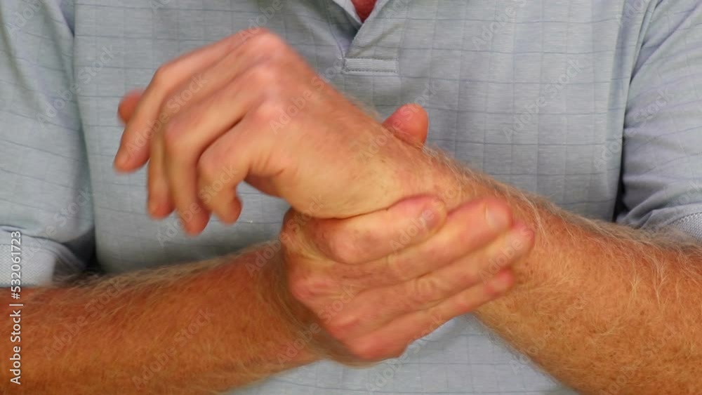 Right hand of a mature caucasian man wearing a blue shirt self massaging his left wrist joint to help relieve pain. Left wrist-joint self-massaged to help pain by mature male in a blue shirt close-up. Right hand of a mature caucasian man wearing a blue shirt self massaging his left wrist joint to help relieve pain. Left wrist-joint self-massaged to help pain by mature male in a blue shirt close-up.