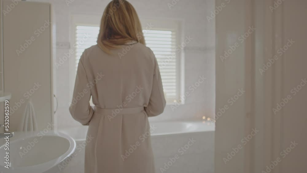 Beautiful woman walking towards filled bathtub and opening her robe