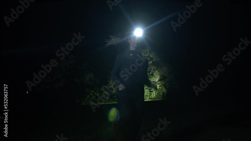 A woman runs in the middle of nature with her headlamp at night