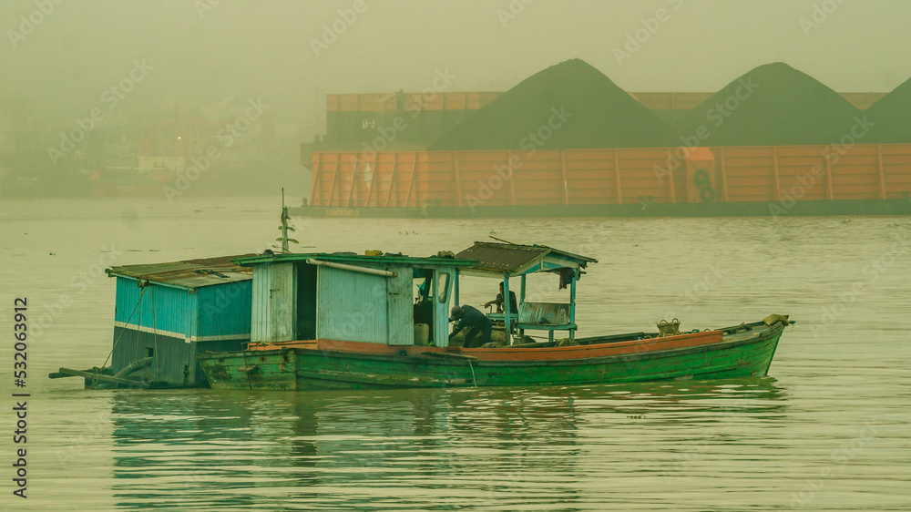 Sand miner activity at Mahakam River, Samarinda in the morning. Wooden boat take up the sand from the bottom of Mahakam River in the morning with barge of coal in the background.