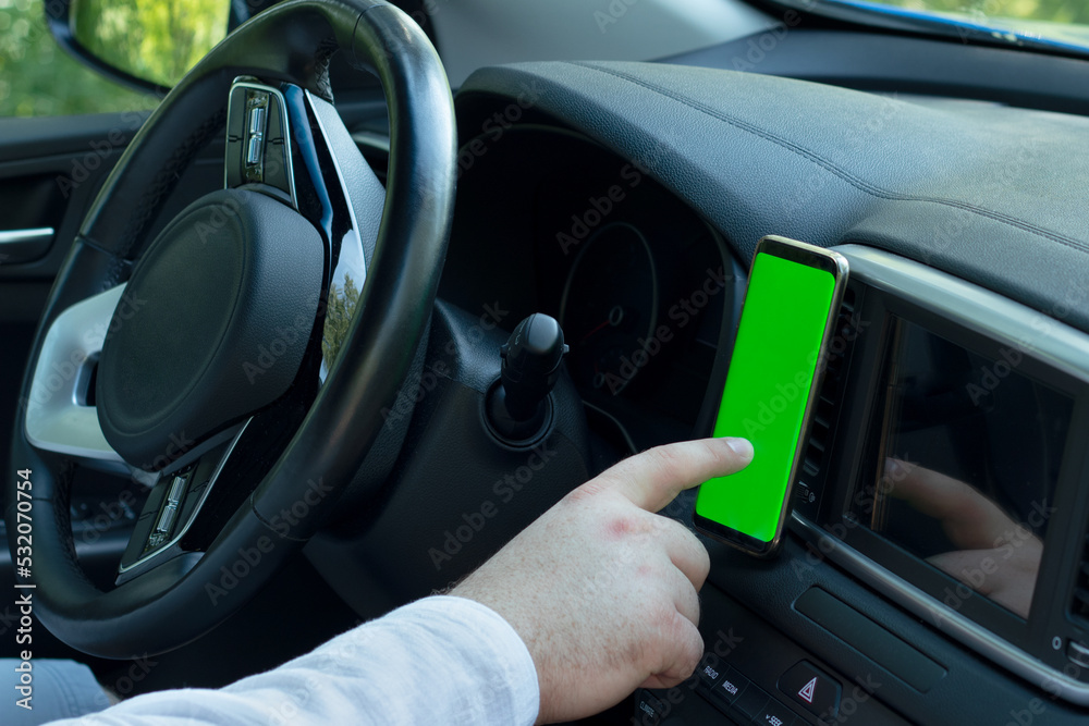 Male hand uses smart phone with blank green screen inside car. Searching location via gps navigator application. Concept for communication technology.