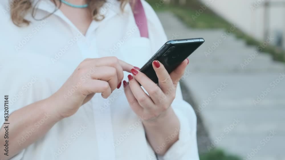 Happy young business woman walking in city street looking into mobile phone smartphone screen chatting online in net smiling answering message in social media using gadget device Happy young business woman walking in city street looking into mobile phone smartphone screen chatting online in net smiling answering message in social media using gadget device