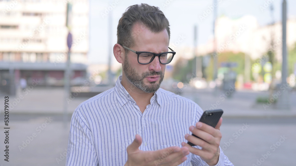 Upset Young Adult Man Reacting to Loss on Smartphone Outdoor Upset Young Adult Man Reacting to Loss on Smartphone Outdoor