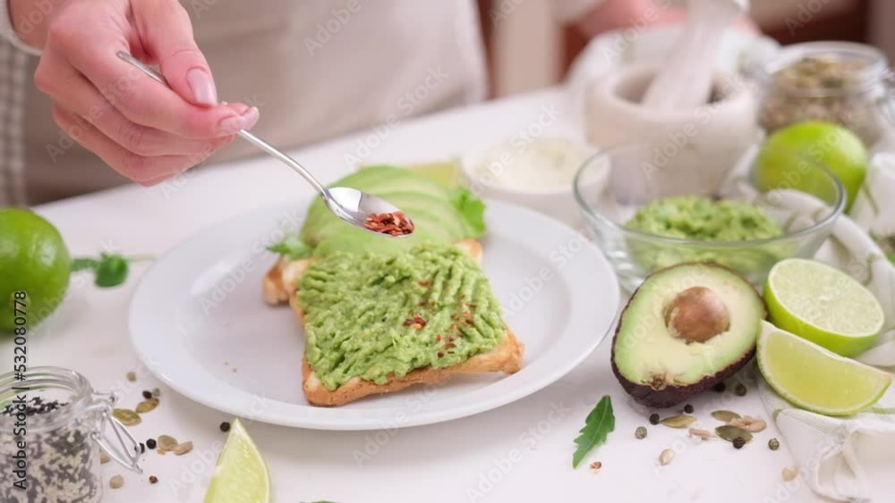 Cooking avocado sandwiches - woman pours spices on a mashed avocado on a toast Cooking avocado sandwiches - woman pours spices on a mashed avocado on a toast