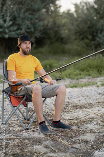 Man fishing with a fishing rod sitting on a chair. Hobby, leisure and people