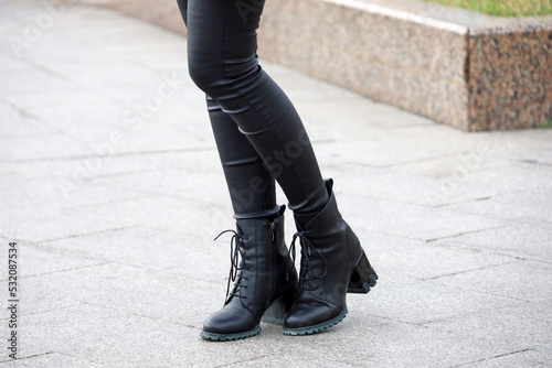 Female legs in black jeans and boots on high heels. Slim girl standing on a street, fashion in autumn city