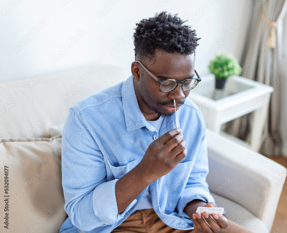 Naklejka premium African-American man using cotton swab while doing coronavirus PCR test at home. man using coronavirus rapid diagnostic test. Young man at home using a nasal swab for COVID-19.