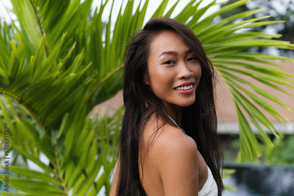 Beautiful asian thai woman with soft smooth clean dark tanned skin posing outdoor in white dress with tropical background Beautiful asian thai woman with soft smooth clean dark tanned skin posing outdoor in white dress with tropical background