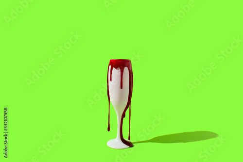 Blood dripping from white glass of champagne on vibrant green background. Minimal Halloween party drinks concept. Pop art.