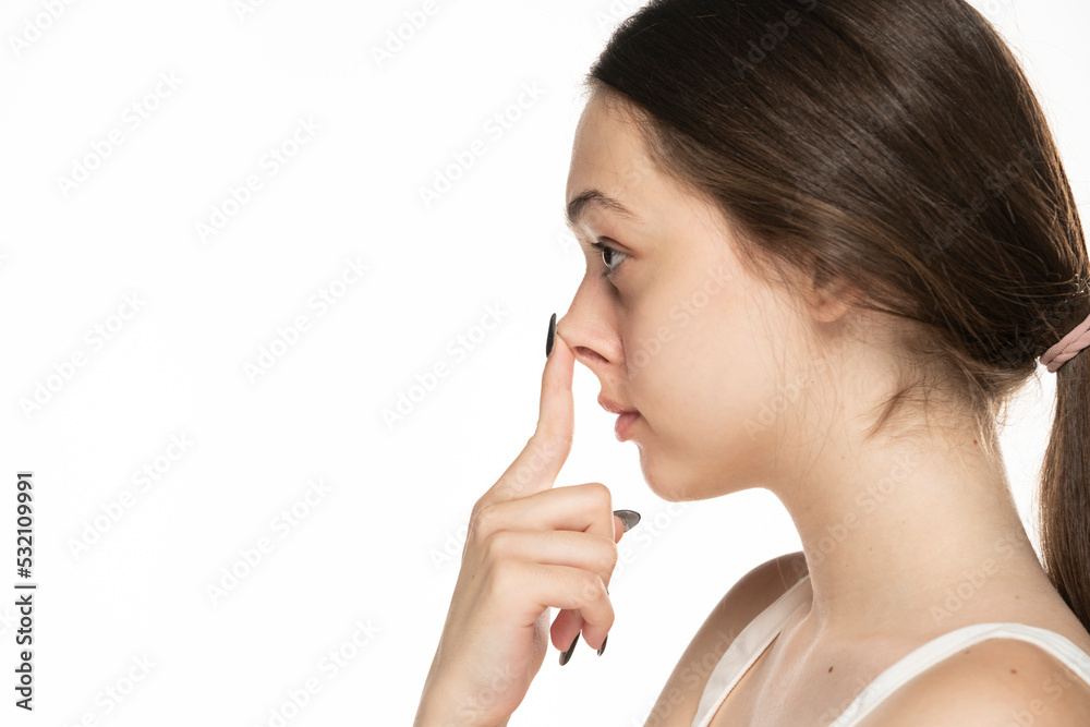 Young serious woman touches her nose with her fingers on a white background. Young serious woman touches her nose with her fingers on a white background.