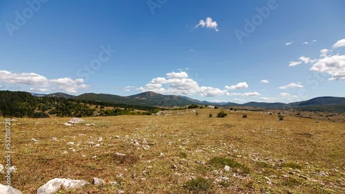 Time lapse shot of a stony grass steppe near Komic with some bushes and trees at sunny noon with some clouds photo