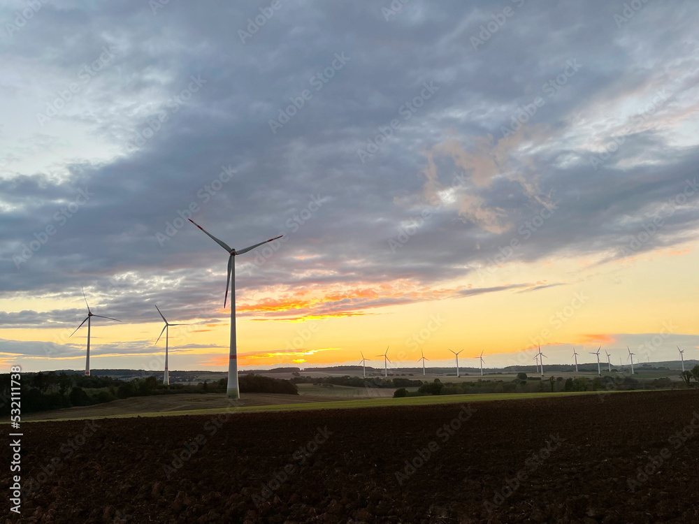 Panoramic view of wind farm or wind park on sundown, with high wind turbines for generation electricity with copy space. Green energy concept.