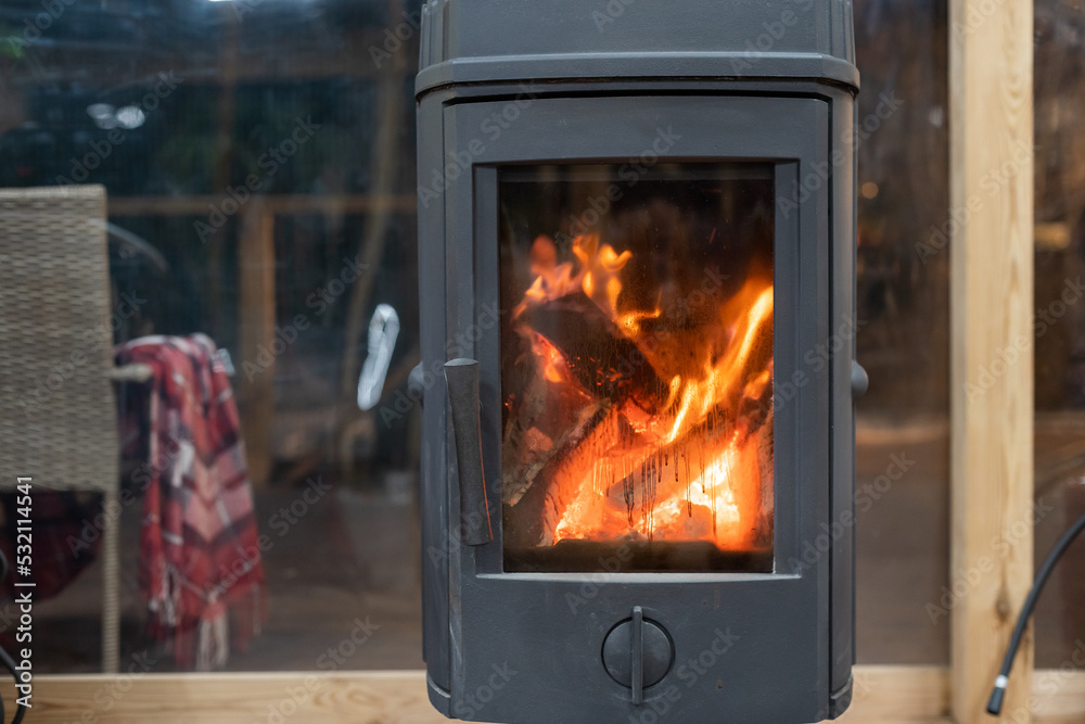 Concept of fireplace with fire at home. Comfortable living room with log wood on top of metal fireside, behind glass door and modern interior design. Concept of fireplace with fire at home. Comfortable living room with log wood on top of metal fireside, behind glass door and modern interior design.