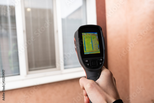 A male hand holds a thermal imager at the window of a house. Search for heat loss in private houses