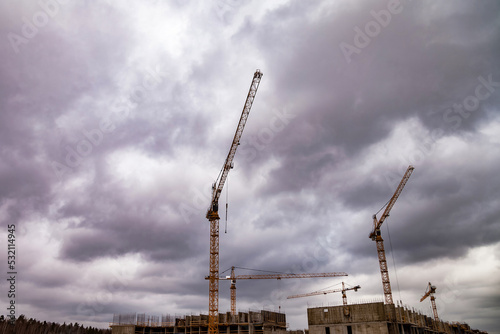 Bottom view of industrial cranes. Construction crane work on creation site against cloudy sky background. Concept of construction of apartment buildings and renovation of housing. Copy space
