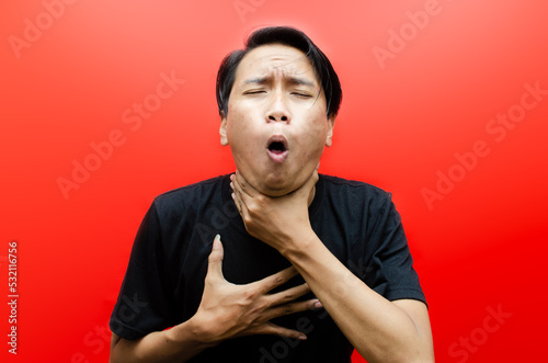Ew. It's so gross. A young Asian man in a t-shirt stands over an empty red background while displaying an expression of dislike and disgust. man is showing vomit gesture.