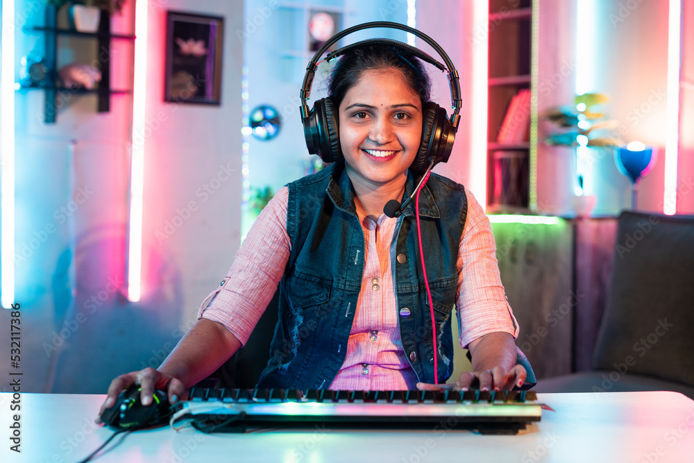 happy girl woman playing video game by talking on headphones while looking camera on neon background - concept of tournament, entertainment and gaming addiction.