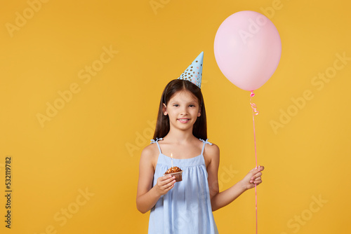 happy little birthday girl with party cone holding cupcake