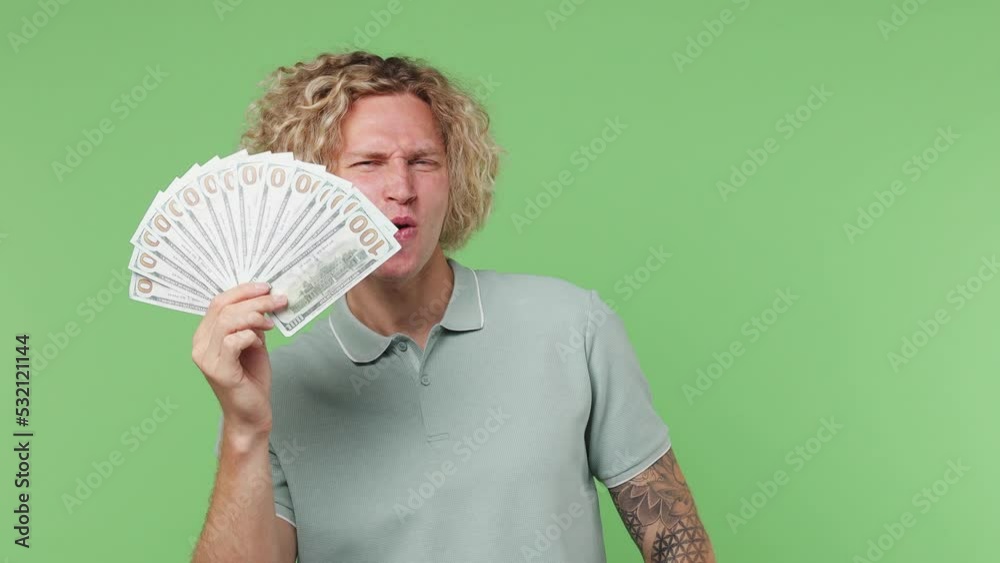 Young blond man 20s he wear blue t-shirt hold in hand fan of cash money in dollar banknotes do winner gesture isolated on plain pastel light green background studio portrait. People lifestyle concept Young blond man 20s he wear blue t-shirt hold in hand fan of cash money in dollar banknotes do winner gesture isolated on plain pastel light green background studio portrait. People lifestyle concept