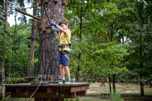 Strong excited young boy playing outdoors in rope park. Caucasian child dressed in casual clothes and sneakers at warm sunny day. Active leisure time with children concept