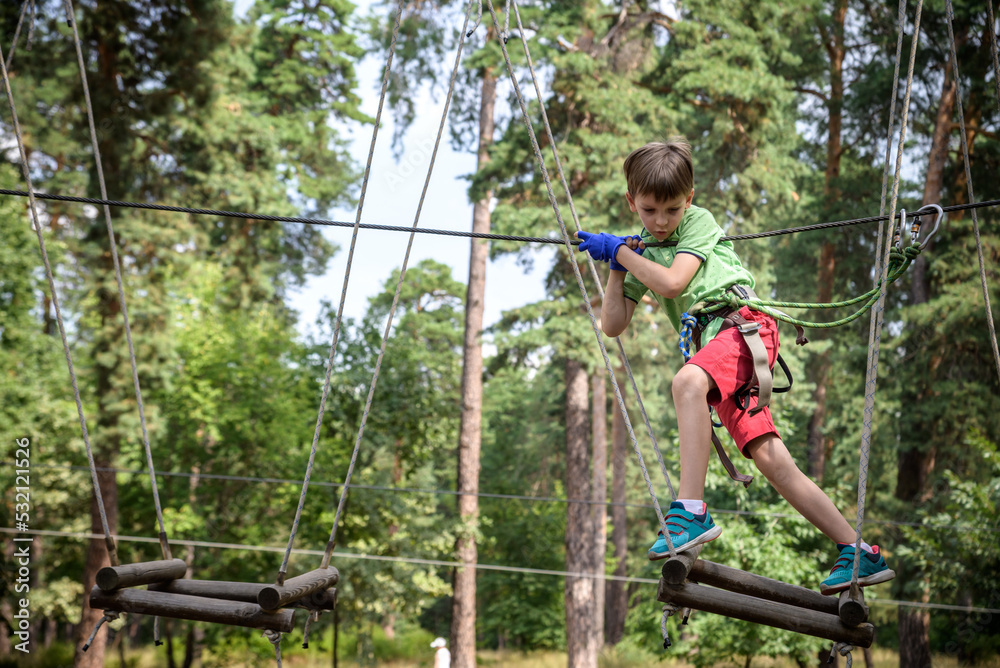 Strong excited young boy playing outdoors in rope park. Caucasian child dressed in casual clothes and sneakers at warm sunny day. Active leisure time with children concept