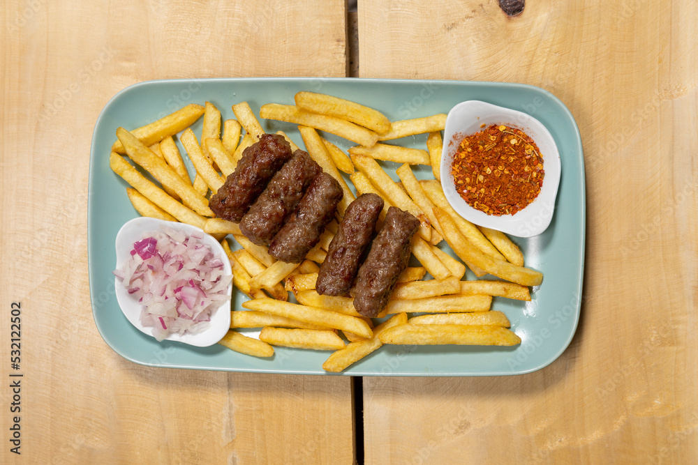Kebabs served on a wooden board with french fries and onion