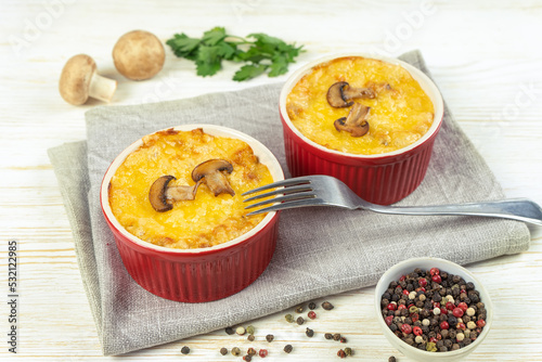 Chicken and mushroom casserole with golden crust, julienne with baked cheese, creamy gratin in portion ramekin clay pot on white wooden background. French cuisine. Top view, flat lay with copy space