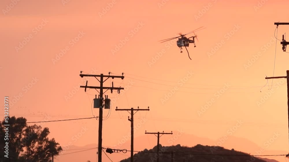 Following a firefighter helicopter flying over power lines, during a hazy sunset Following a firefighter helicopter flying over power lines, during a hazy sunset