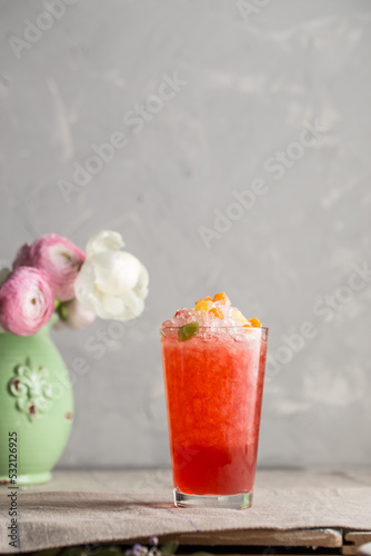 Red summer cocktail with juice, cruched ice and fresh flowers on the table photo