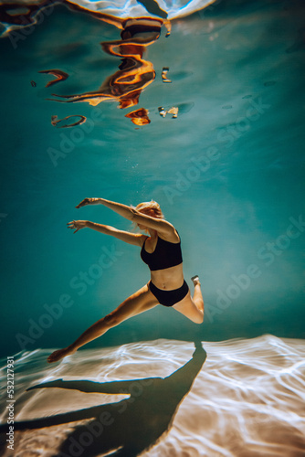 Art work. A slender, tanned girl with an athletic figure and blond hair, in black lingerie, dives and dances underwater in the pool. Aesthetic image for your design or decoration. © Ihor