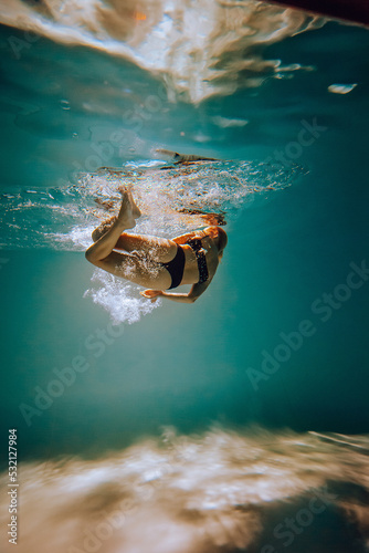 Art work. A slender, tanned girl with an athletic figure and blond hair, in black lingerie, dives and spins underwater in the pool. Aesthetic image for your design or decoration.