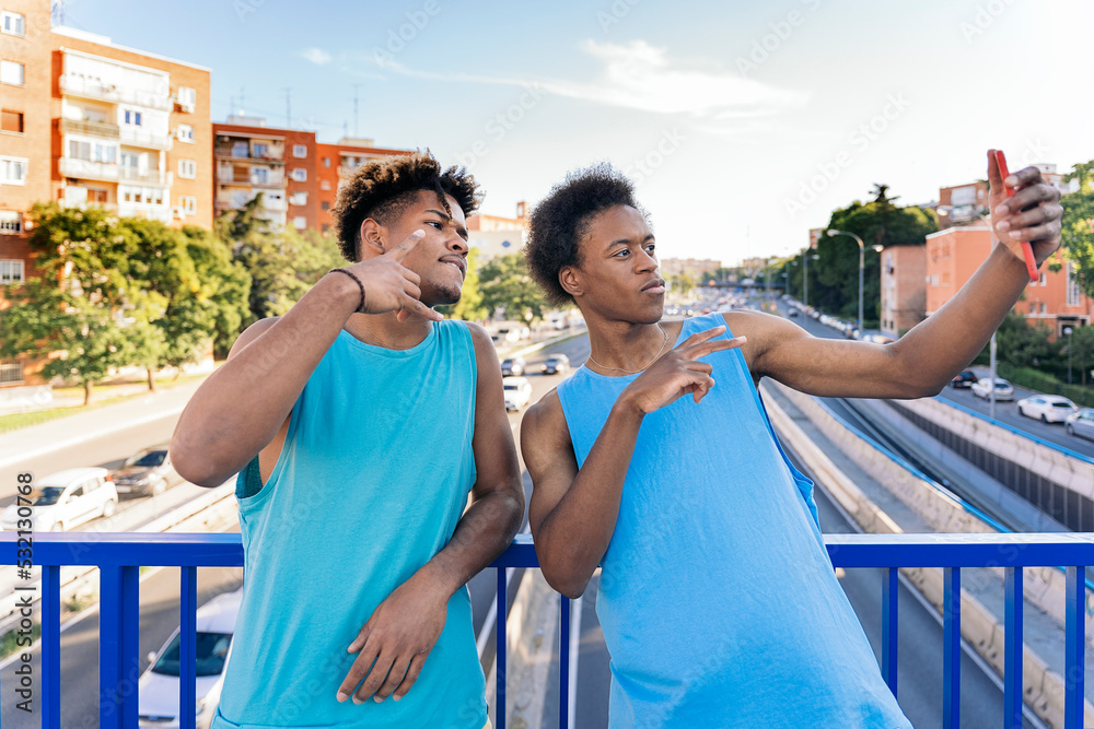 Two young men wearing sleeveless t-shirt taking a selfie on footbridge in the city Two young men wearing sleeveless t-shirt taking a selfie on footbridge in the city
