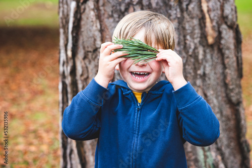 Smiling happy boy portrait hiding behind pine tree needles leaves photo