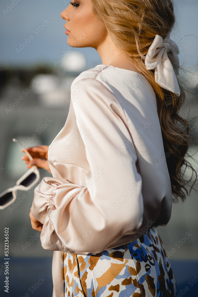 Gorgeous young woman in elegant silk blouse stand on roof terrace with sunglasses sideways closeup. Photo of parisian lady in stylish outfit on sky background. Paris fashion, roof, sky, glamour