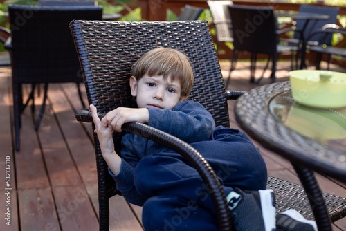 Slika na platnu Unhappy little boy lie bending body on chair at table in cafe on summer terrace