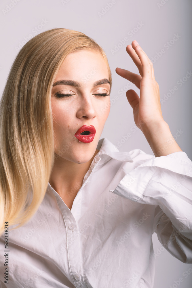 Fashion, style and make-up concept. Close-up studio portrait of beautiful and sexy looking blonde woman with red lipstick and closed eyes making O shape with lips. Model wearing white shirt Fashion, style and make-up concept. Close-up studio portrait of beautiful and sexy looking blonde woman with red lipstick and closed eyes making O shape with lips. Model wearing white shirt