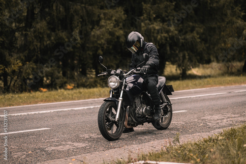 male motorcyclist in a warm jacket and helmet in cold autumn weather on the road with a motorcycle cafe racer