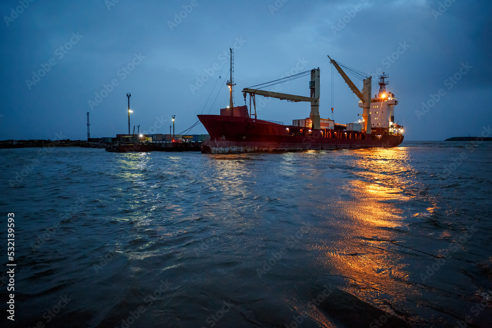 Cargo ship near the pier. Evening industrial seascape. Sea freight and supply in the North-East of Russia. Anadyr estuary, Chukotka, Russian Far East.