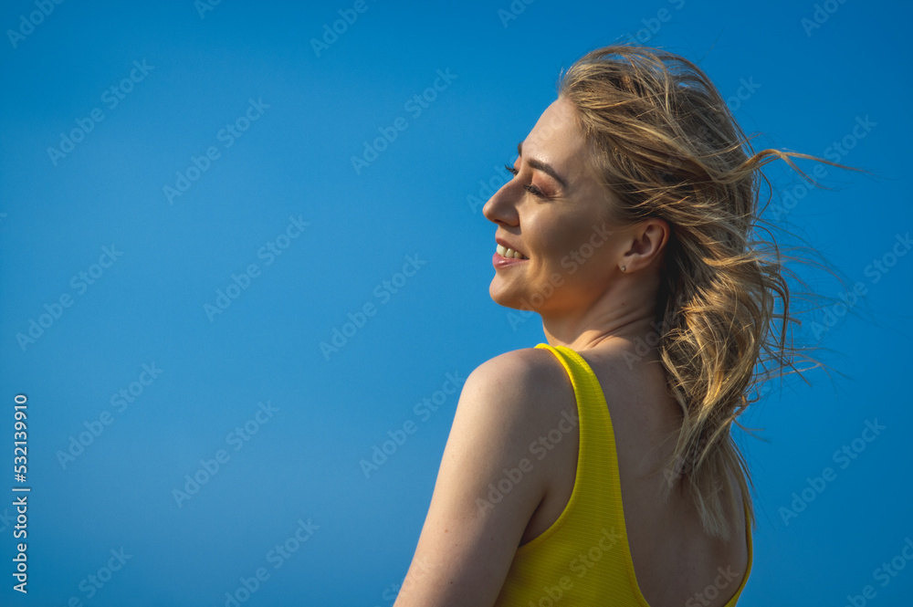 closeup sideview of smiling attcative caucasian woman in yellow sundress looking side against ultramarine sky closeup sideview of smiling attcative caucasian woman in yellow sundress looking side against ultramarine sky