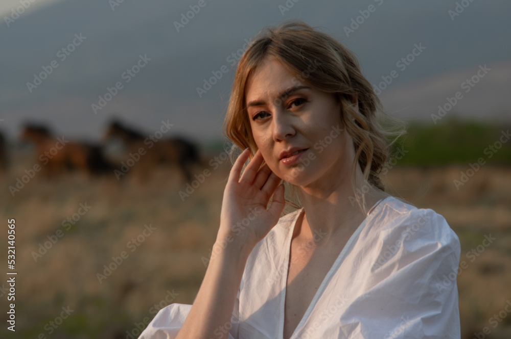 selective fous on portrait of a attractive woman in white sundress on the backgroun of blurred herd of horses selective fous on portrait of a attractive woman in white sundress on the backgroun of blurred herd of horses