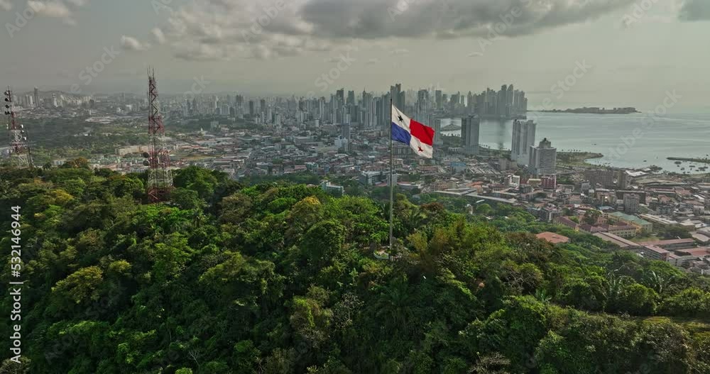 Panama City Aerial v67 cinematic low level flyover ancon hill with wind blowing the national flag on hilltop with coastal downtown cityscape in the background - Shot with Mavic 3 Cine - March 2022