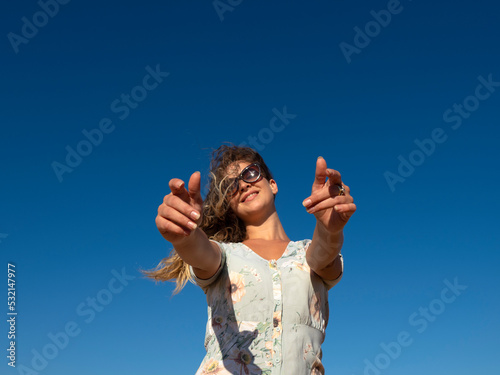 Smiling woman outstretching arms against blue sky