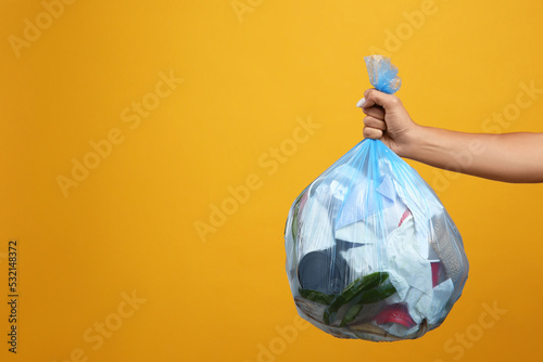 Woman holding full garbage bag on yellow background, closeup. Space for text photo