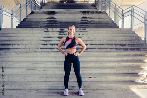 Cropped shot portrait of a happy young sportswoman standing outdoors. Young female athlete smiling at the camera while standing with her hands on her hips. © Jelena Stanojkovic