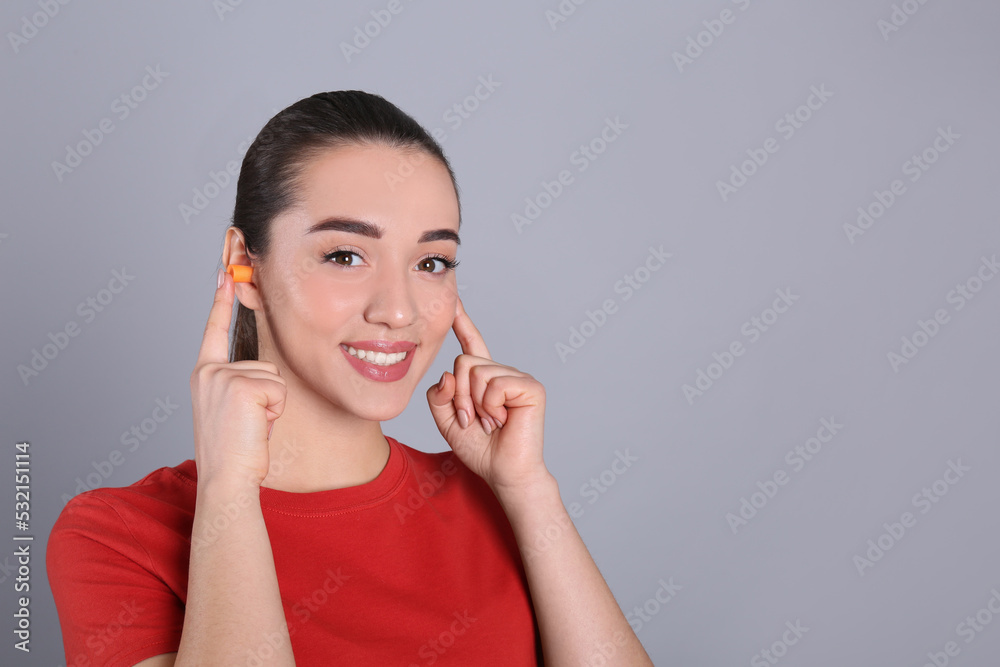 Young woman inserting foam ear plugs on grey background. Space for text Young woman inserting foam ear plugs on grey background. Space for text