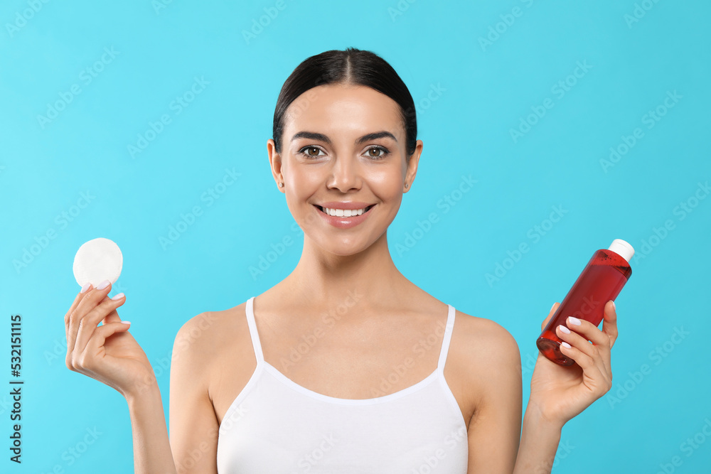 Young woman with micellar water and cotton pad on light blue background Young woman with micellar water and cotton pad on light blue background