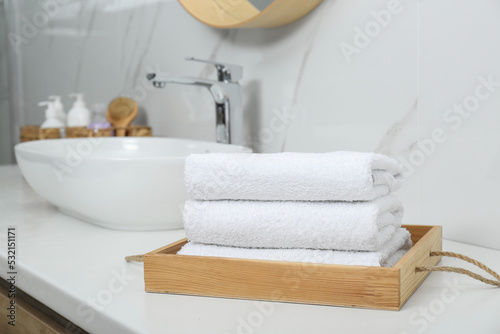 Wooden tray with rolled bath towels on white table in bathroom