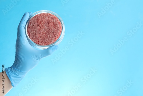 Φωτογραφία Scientist holding Petri dish with minced lab grown meat on light blue background, closeup